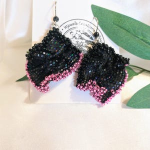 May include: Black and pink beaded earrings with a floral design. The earrings are handmade and have a silver hook.