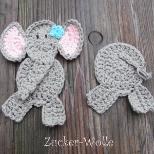 Könnte beinhalten: Zwei gehäkelte Elefanten-Applikationen. Eine ist komplett mit grauer Wolle, rosa Innenohren und einer blauen Blume. Die andere ist eine passende graue Applikation. Der Text "Zucker-Wolle" steht unten.