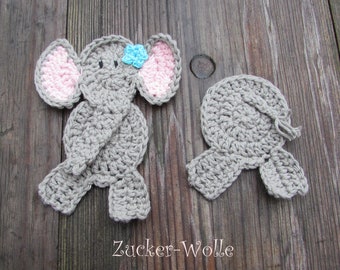 Puede incluir: Dos apliques de elefante de ganchillo. Uno está completo con hilo gris, orejas internas rosas y una flor azul. El otro es un aplique gris a juego. El texto "Zucker-Wolle" está en la parte inferior.