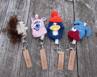 Puede incluir: Cuatro fundas para llaves de ganchillo con anillas metálicas y etiquetas de papel marrón con la inscripción Schlüsseltasche. Los personajes incluyen una criatura marrón peluda, un monstruo rosa de un ojo, un pingüino azul con gorro naranja.