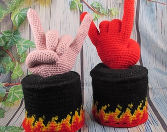 Puede incluir: Dos fundas de papel higiénico de ganchillo, cada una con un gesto de mano en la parte superior. Una funda es negra con un patrón de llamas rojas y amarillas en la base y una mano rosa claro. La otra es negra con llamas y una mano roja.