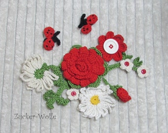 Puede incluir: Aplique de flores de ganchillo con rosas rojas, margaritas blancas, hojas verdes y mariquitas rojas. El aplique está sobre un fondo blanco texturizado. El texto "Zucker-Wolle" es visible en la esquina inferior izquierda.