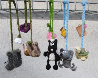 Puede incluir: Un conjunto de cinco adornos de ganchillo con forma de animales colgados de una rejilla metálica. Las figuras incluyen un perezoso gris, un perezoso marrón, una mofeta blanca y negra, un ratón gris y una tortuga amarilla y verde.