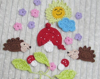 May include: Crocheted woodland-themed embellishments, including a red mushroom with white spots, a smiling yellow sun, blue cloud, brown hedgehogs, pink and purple flowers, and green leaves. The text "Zucker-Wolle" is visible.