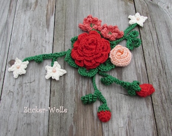 Puede incluir: Una guirnalda de ganchillo con flores rojas, rosas y blancas, hojas verdes y fresas rojas. La guirnalda está sobre un fondo de madera. El texto "Zucker-Wolle" es visible en la esquina inferior izquierda de la imagen.