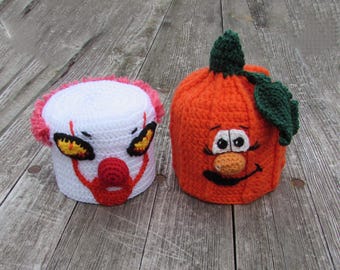 Puede incluir: Dos fundas de ganchillo para rollos de papel higiénico. Una es blanca con pelo rojo, nariz roja y ojos amarillos que recuerdan a un payaso. La otra es naranja con tallo y hoja verdes, con una cara de dibujos con nariz beige y sonrisa.