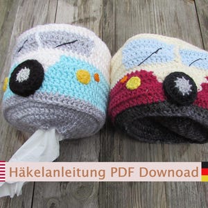 May include: Two crocheted toilet paper covers shaped like buses, one in light blue and white and the other in red and cream. Each features black wheels, yellow headlights, and light blue windshields with black stitched wipers. One holds a tissue.