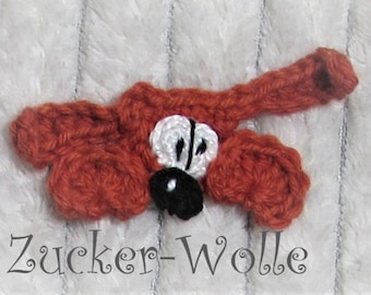 May include: A crocheted ladybug with a red body, white wings, and black spots. The ladybug is on a white fuzzy background. The text "Zucker-Wolle" is visible below the ladybug.