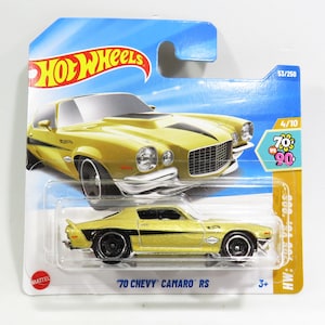 May include: A gold 1970 Chevrolet Camaro RS Hot Wheels die-cast car in a blue and yellow package. The car has black stripes and "70 CHEVY CAMARO RS" printed on the package. The package also has "HW: 500, SA 5174" and "70's vs 90's" printed on it.