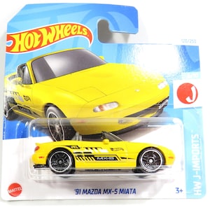 May include: A yellow 1991 Mazda MX-5 Miata Hot Wheels die-cast car with black racing stripes and a black interior. The car is on a blue and white card with the Hot Wheels logo and the words 'HW J-IMPORTS' and '120/250'.