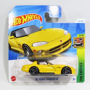 Puede incluir: Un coche de juguete fundido a presión amarillo '92 Dodge Viper RT/10 sobre una tarjeta azul y blanca. El coche tiene ruedas negras y un techo negro. El embalaje incluye el logotipo de Hot Wheels y el texto "HW Exotics".