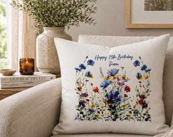 May include: A cream-colored throw pillow with a floral design and the text "Happy 75th Birthday Pam." The pillow features a colorful wildflower arrangement in shades of blue, purple, red, and yellow, creating a decorative accent for home decor.
