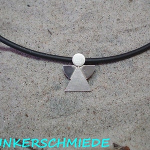 Könnte beinhalten: Eine silberne Engels-Anhänger-Kette mit einem schwarzen Band. Der Engel besteht aus einfachen geometrischen Formen.