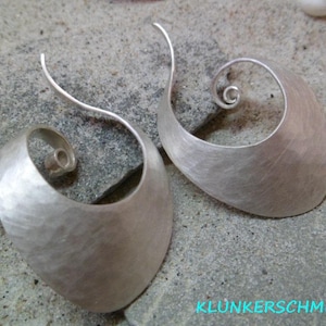 Könnte beinhalten: Ein Paar silberne Ohrringe mit gehämmerter Oberfläche und einem Spiraldesign. Die Ohrringe sind von Klunkersschmiede.