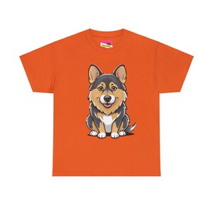 May include: Orange t-shirt featuring a cartoon corgi. The corgi is predominantly black and tan, sitting and facing forward. The shirt is a simple, short-sleeved crew neck style.  The design is centered on the shirt.
