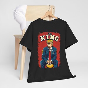 May include: Black t-shirt with a graphic of a man sitting on a golden toilet. The graphic has the text "The King" above the man.