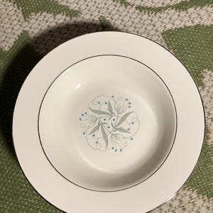 May include: A white ceramic soup bowl with a blue and gray floral design and a gold rim.
