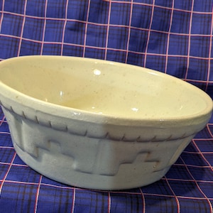 May include: A large, white ceramic bowl with a blue glaze and a decorative pattern around the rim. The bowl is slightly chipped on the rim.