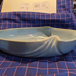 May include: A light blue ceramic bowl with a wavy, organic shape. The bowl is designed to resemble a draped fabric.