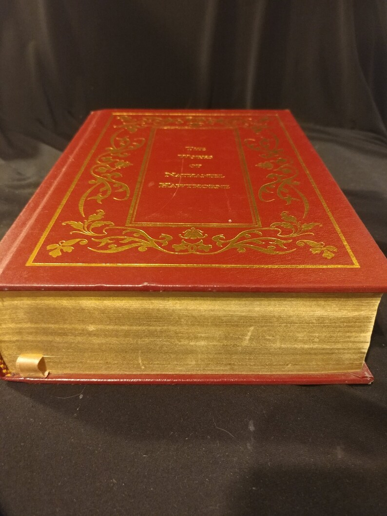 Pode incluir: Um livro encadernado em couro vermelho com detalhes dourados e o t&iacute;tulo "The Writings of Nathaniel Hawthorne" na capa.