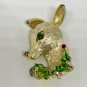 May include: Gold-tone reindeer brooch with green holly leaves and red berries. The reindeer has a green rhinestone eye.