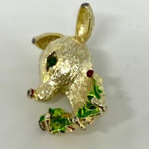 May include: Gold-tone reindeer brooch with green and red enamel accents. The reindeer is holding a sprig of holly in its mouth.