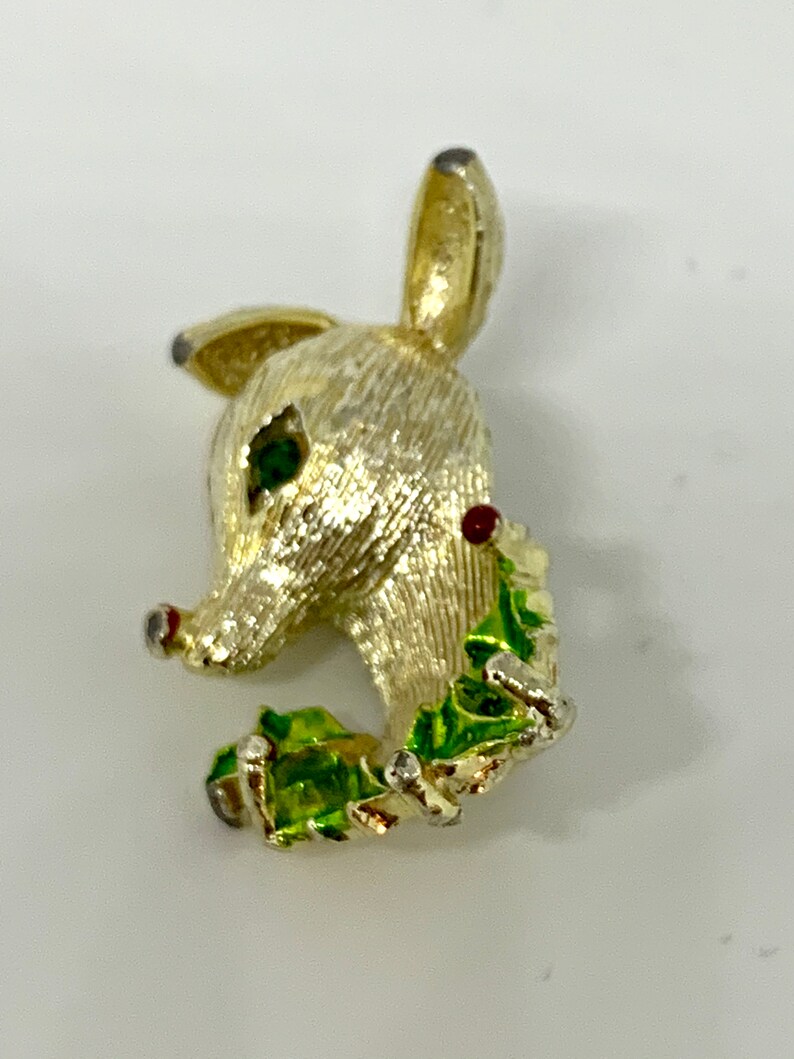 May include: Gold-tone reindeer brooch with green and red enamel accents. The reindeer is holding a sprig of holly in its mouth.