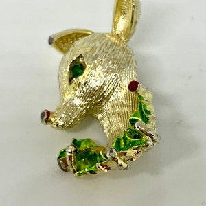 May include: A gold-tone reindeer brooch with green and red enamel accents. The reindeer is holding a sprig of holly in its mouth.