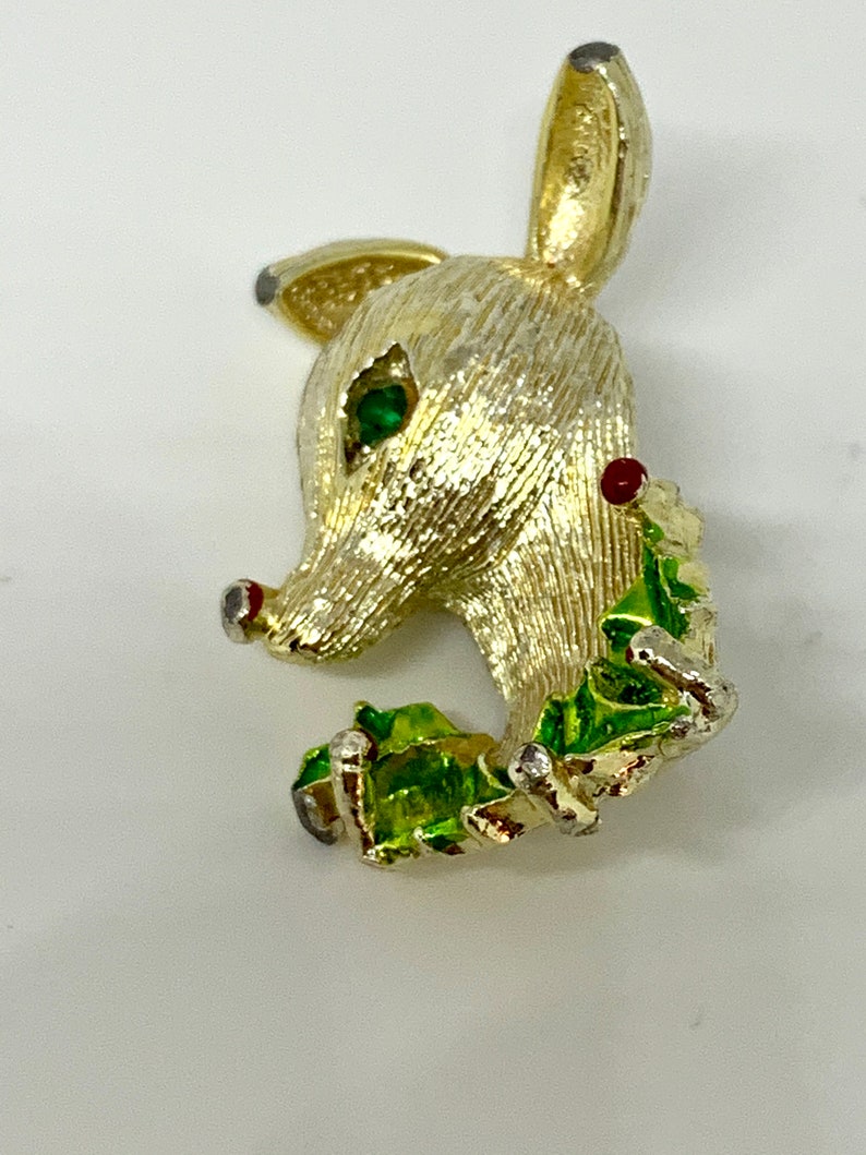 May include: Gold-tone reindeer brooch with green and red enamel holly leaves and red and clear rhinestones.