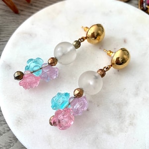 May include: A pair of gold tone dangle earrings with clear glass beads and pastel pink, blue, and purple flower-shaped beads.