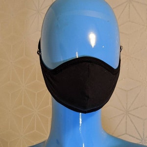 May include: A black face mask with a curved design, displayed on a blue mannequin head. The mask has a black trim and adjustable ear loops. The background features a geometric pattern.
