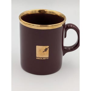 May include: A deep burgundy ceramic mug featuring a metallic gold rim and a matching gold square logo on the front. The logo contains a stylised symbol and the text "SEQUENT" printed in a clean, sans-serif font. The mug has a curved handle.