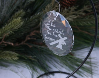 May include: A clear glass Christmas bauble with the words "It's the reason for his season" and a silhouette of a person on a cross.