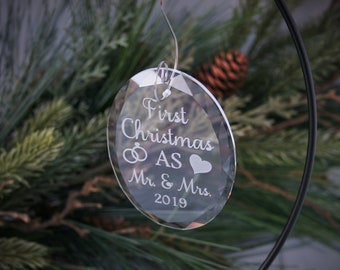 May include: A clear glass Christmas bauble with the text "First Christmas as Mr. & Mrs. 2019" engraved on it. The bauble features a ring and a heart.