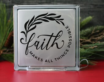 May include: A white glass block with a black floral design and the text "faith makes all things possible".