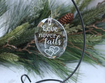 May include: A clear glass bauble with the words "Love never fails" etched on it. Two hearts are also etched on the bauble.