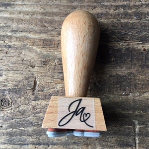 K&ouml;nnte beinhalten: Holzstempel mit einem schwarzen Stempelkissen und einem individuellen Design, das "Ja" mit einem Herzen sagt.