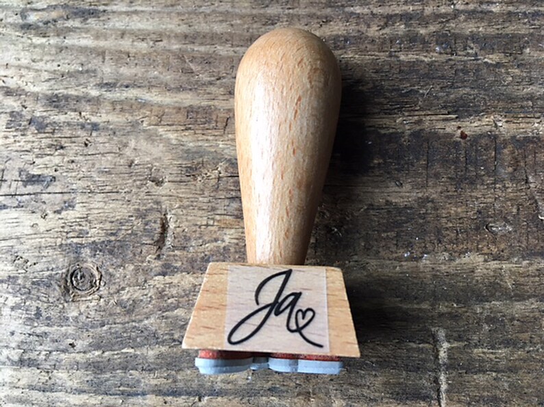 K&ouml;nnte beinhalten: Holzstempel mit einem schwarzen Stempelkissen und einem individuellen Design, das "Ja" mit einem Herzen sagt.