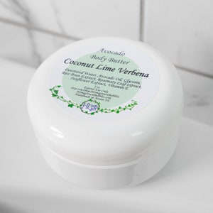 May include: A white, round container of Avocado Body Butter with a label that reads "Coconut Lime Verbena." The label lists ingredients like avocado oil and vitamin E. The container is 5 oz.