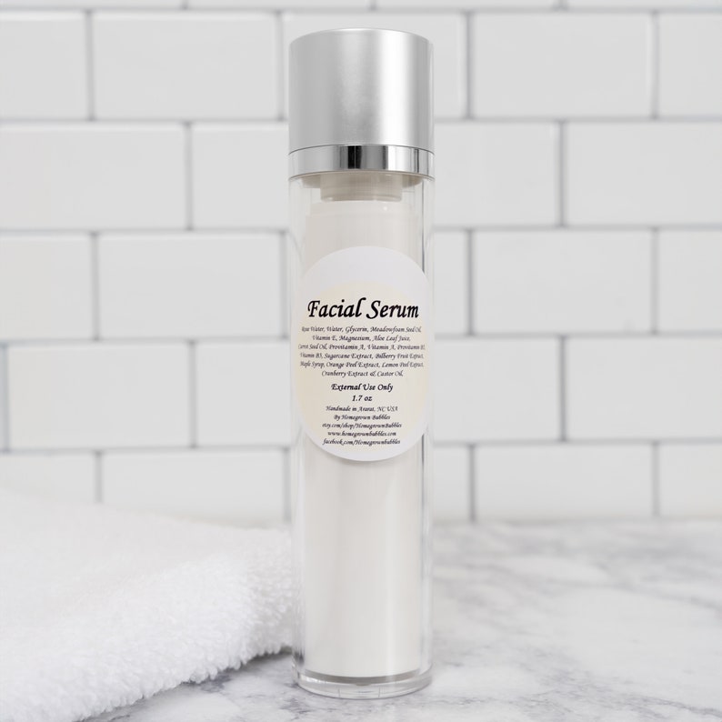 Pu&ograve; includere: Una bottiglia di vetro trasparente con un tappo argentato e un'etichetta bianca che recita "Facial Serum". L'etichetta elenca gli ingredienti, tra cui acqua di aloe vera, glicerina, magnesio, olio di semi di meadowfoam, vitamina E, magnesio, succo di foglie di aloe vera, vitamina C, pantenolo, vitamina A, provitamina B5 e olio. L'etichetta indica anche "Uso esterno solo" e "1,7 oz".