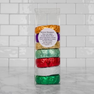 May include: A clear plastic container with six colorful shower steamers wrapped in foil. The container has a label that reads "Shower Steamers" and includes instructions for use.