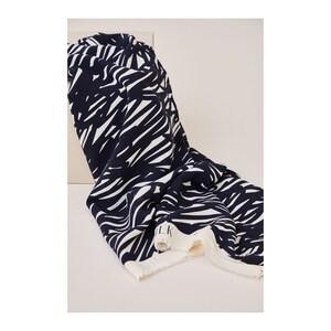 May include: A navy blue and white fabric with a bold, abstract pattern. The fabric is folded and draped over a white surface. The fabric has a raw edge.