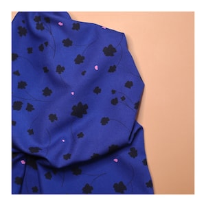 May include: Blue fabric with a black and pink floral pattern. The fabric is folded and has a soft, smooth texture.