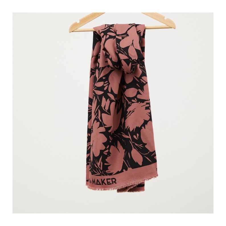 Puede incluir: Una bufanda de color rosa y negro con estampado floral y la palabra "Maker" impresa en el borde inferior.