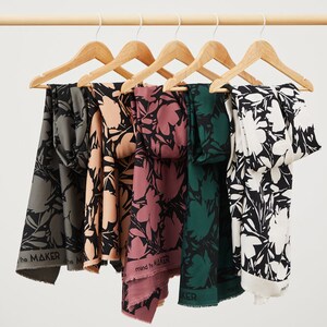 Puede incluir: Cinco muestras de tela colgadas de perchas de madera. La tela es negra con un estampado floral blanco. Las muestras son de diferentes colores: verde, rosa, melocot&oacute;n, gris y blanco.