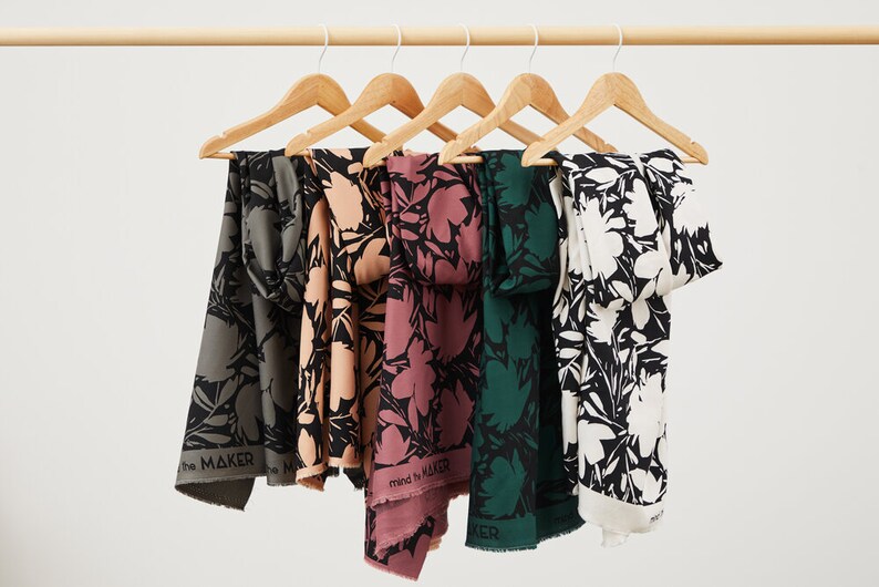 Puede incluir: Cinco muestras de tela colgadas de perchas de madera. La tela es negra con un estampado floral blanco. Las muestras son de diferentes colores: verde, rosa, melocot&oacute;n, gris y blanco.