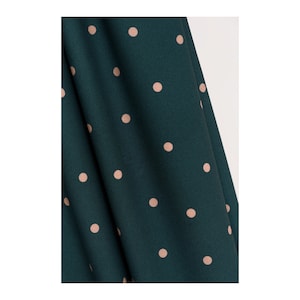 May include: A close-up of a dark green fabric with a pattern of small, light pink polka dots.