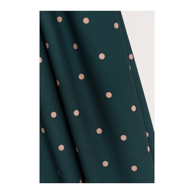 May include: A close-up of a dark green fabric with a pattern of small, light pink polka dots.