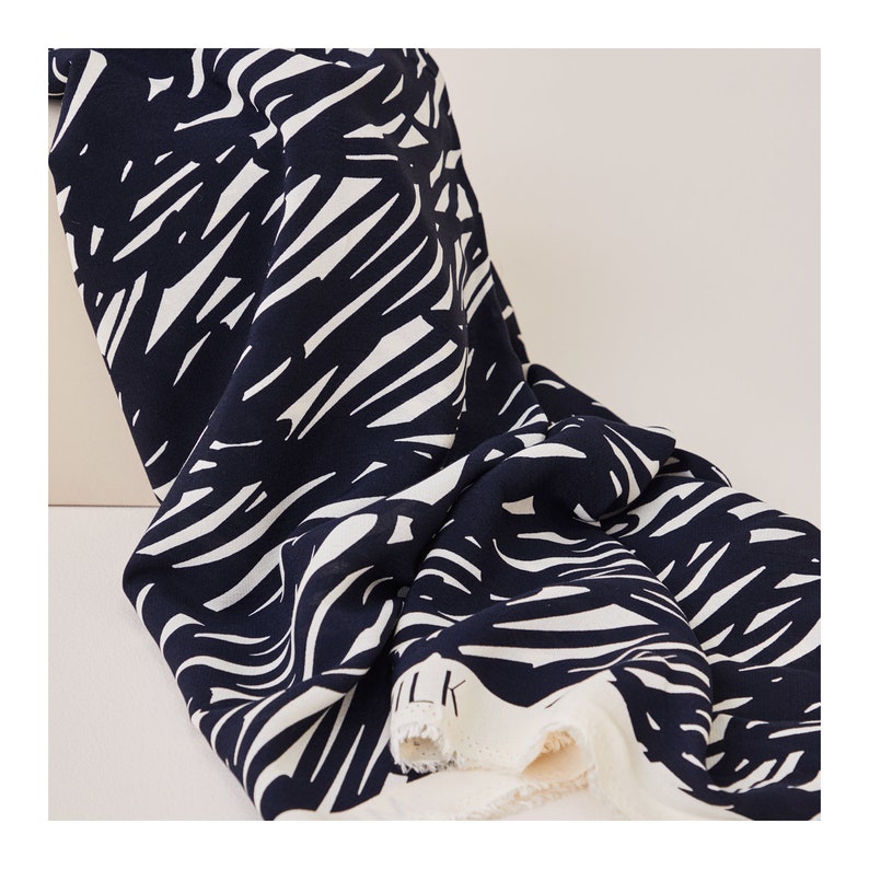 May include: Black and white abstract print fabric with a textured surface. The fabric is folded and the edge is visible.