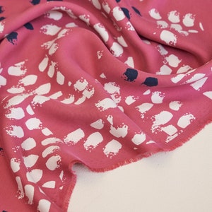 Pu&ograve; includere: Tessuto rosa con una stampa astratta bianca e blu navy. Il tessuto &egrave; piegato e i bordi sono sfilacciati.